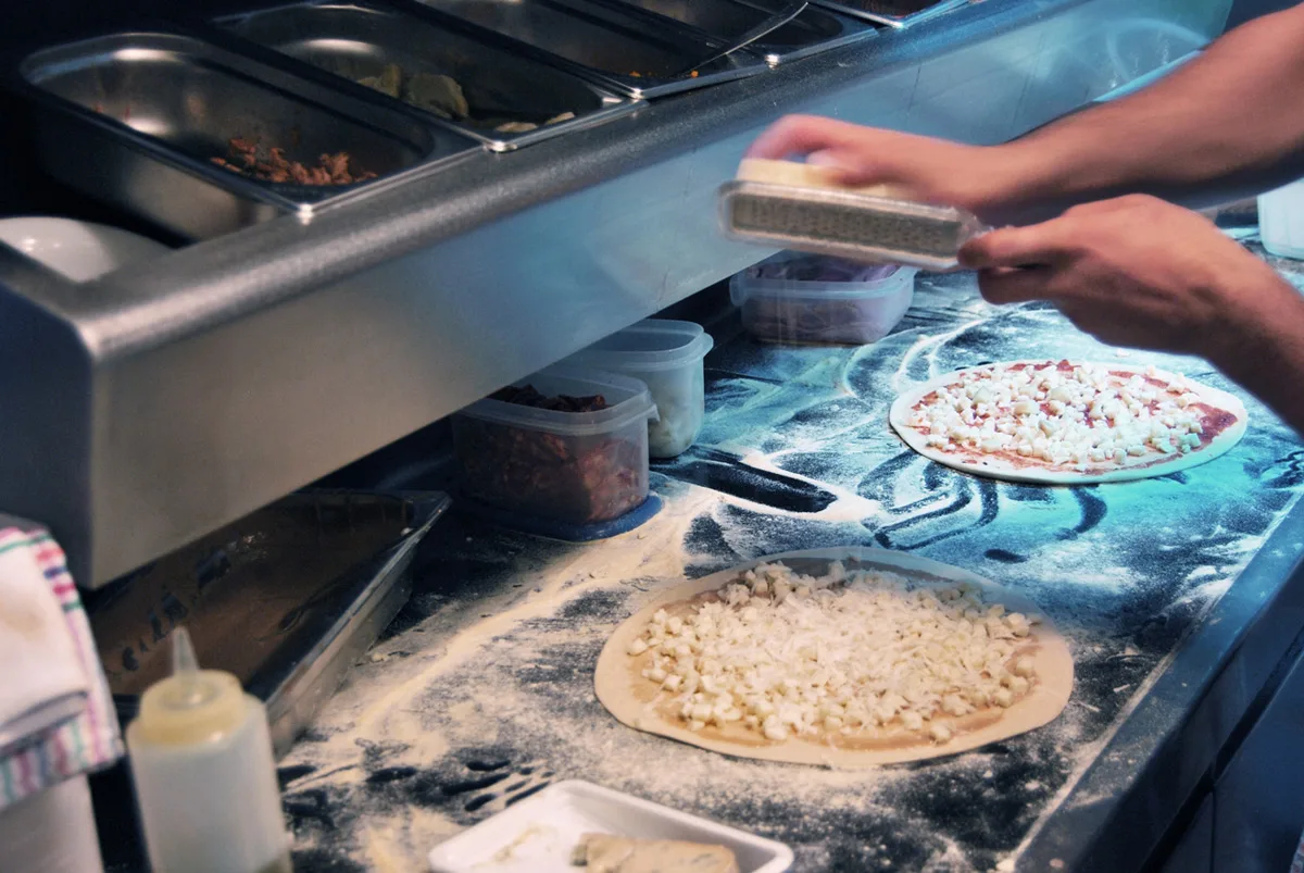 Mans escampant formatge damunt una base de pizza al taulell enfarinat
