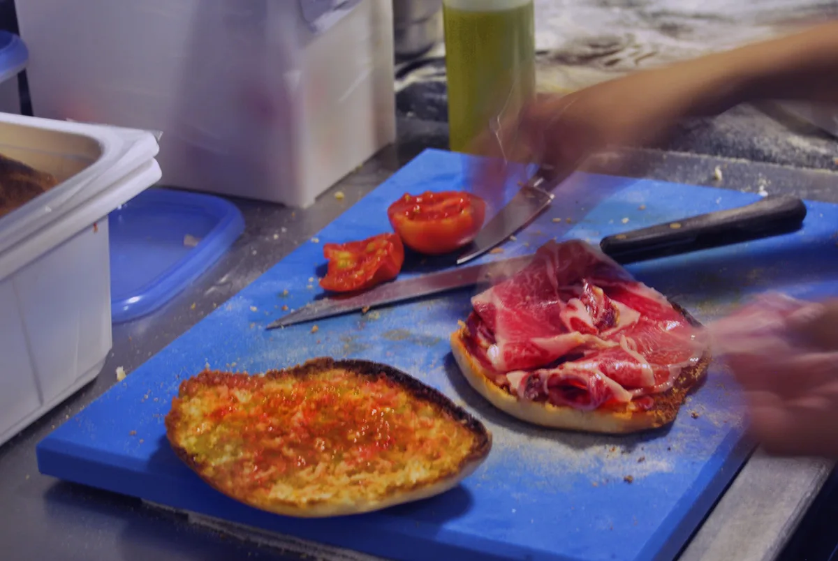 Pa amb tomàquet i llesques de pernil damunt d'una taula de tallar blava