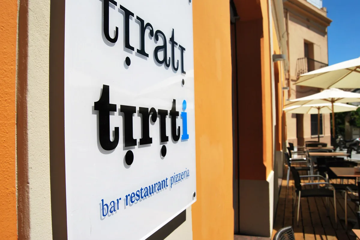 Rètol del Tirati Tiriti a la paret, amb la terrassa i els para-sols de dia