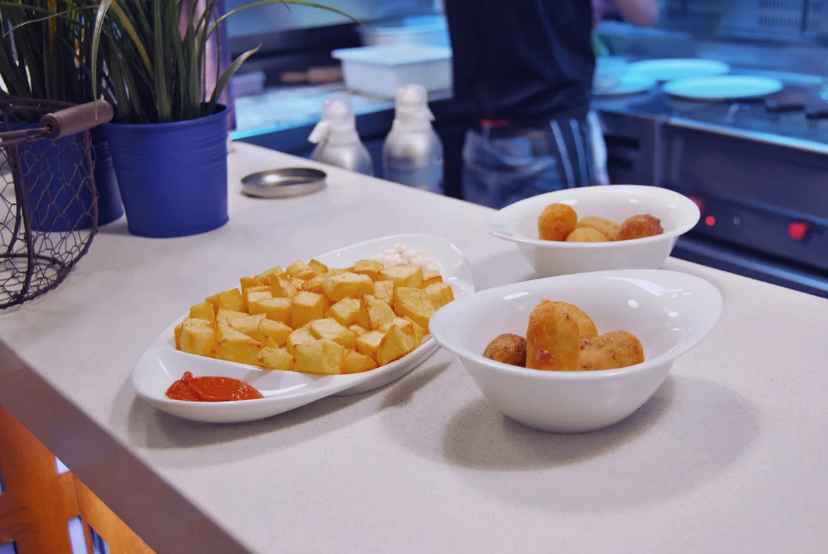 Patates braves amb salsa i un bol de croquetes a la barra
