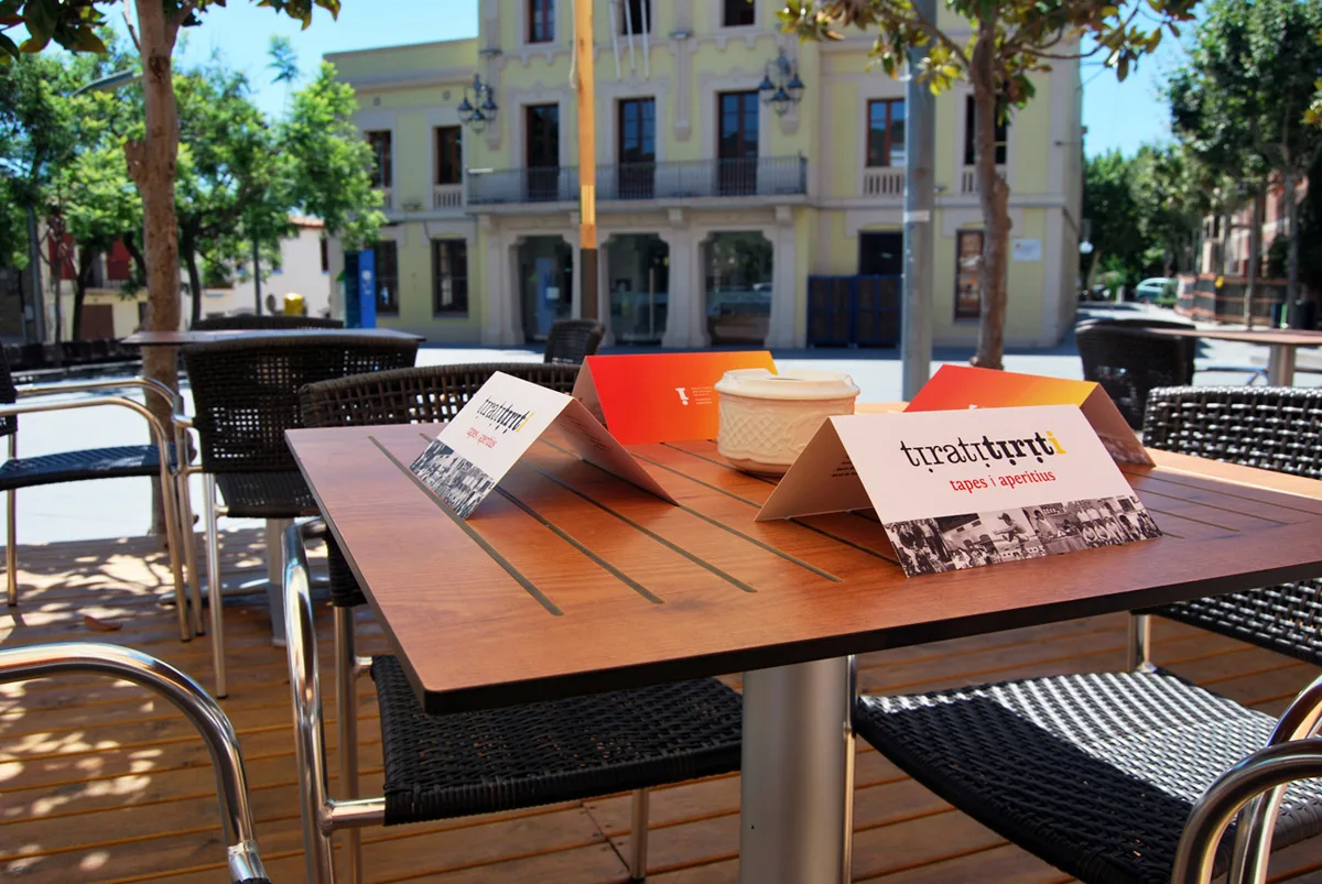 Taula de fusta de la terrassa a la plaça, de dia, amb l'edifici de l'Ajuntament al fons